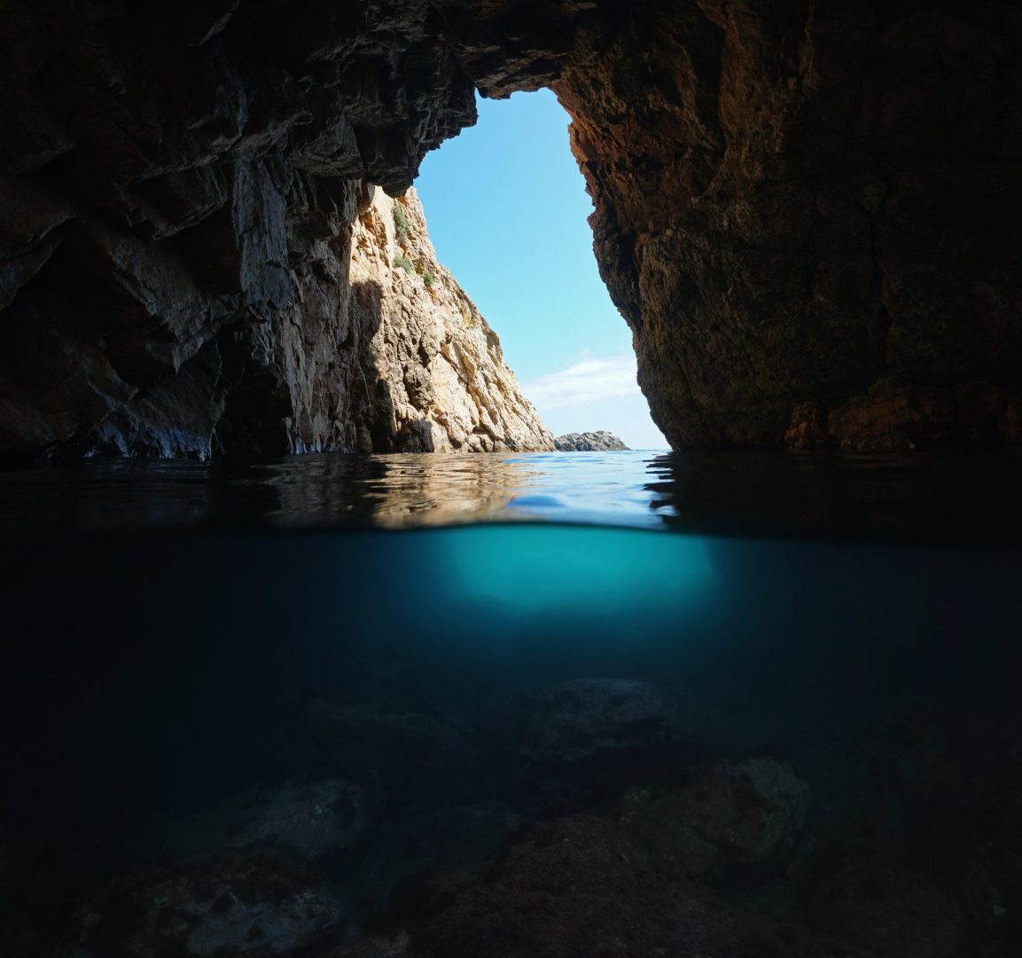 Under a rocky natural arch on the shore of the Mediterranean sea, split view over and underwater, Spain, Costa Brava, Catalonia, Palamos, Cala Foradada